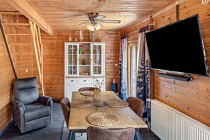Interior em madeira com uma mesa de jantar, cadeiras, uma televisão e um armário com portas de vidro.