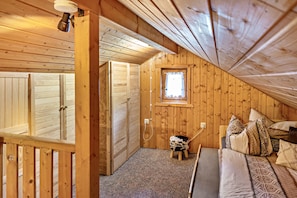 Ein Holzinnenraum mit einem Bett, Kissen, einem kleinen Hocker, einem Fenster und einer Tür.