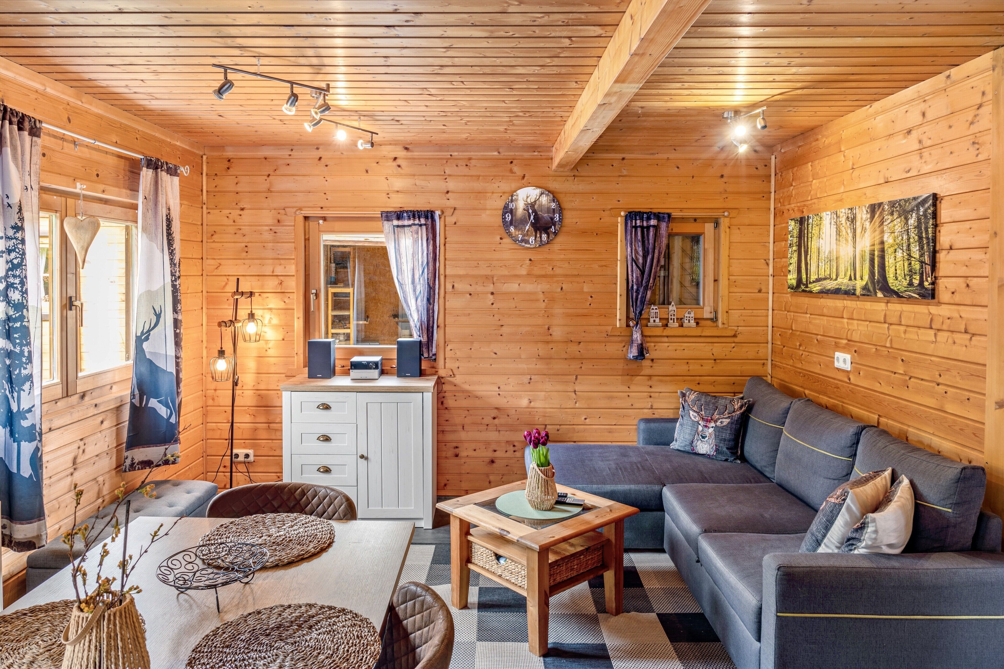 A cozy cabin interior with a wooden ceiling, a sofa, a dining table, and a television.