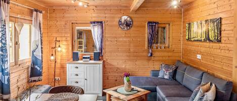 A cozy cabin interior with a wooden ceiling, a sofa, a dining table, and a television.