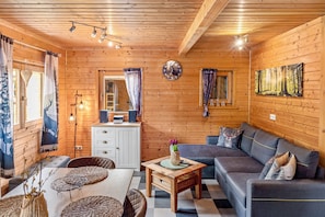 En mysig stuga med träpanel i taket, en soffa, ett matbord och en tv.