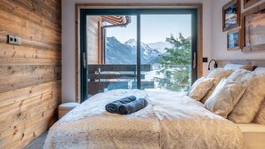 Ein Schlafzimmer mit großem Fenster, Holzwänden, einem Bett mit Decke und Kissen sowie Bergblick.