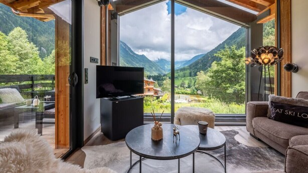Ein modernes Wohnzimmer mit großem Fenster, Flachbildfernseher, einer Couch und einem Couchtisch.