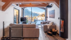 Ein gemütliches Wohnzimmer mit einer Couch, einem Kamin, einem Fernseher und Blick auf die Berge.