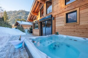 A wooden cabin with a hot tub and a snow-covered deck.