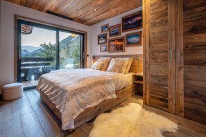 A bedroom with a large bed, wooden ceiling, and a view of mountains through a sliding door.
