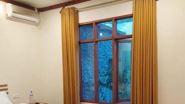 A hotel room with a wooden floor, a bed, a window with curtains, and an air conditioning unit. - Oi Beach (Maamigili)