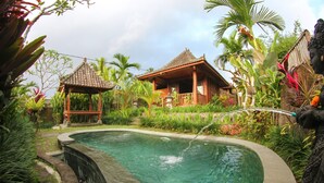 A swimming pool with a wooden gazebo and a traditional house in a tropical garden setting.