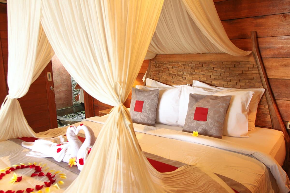 Uma cama com dossel, almofadas e um arranjo de toalhas e flores em formato de coração.