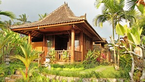 A traditional wooden structure with a tiled roof, surrounded by lush greenery and palm trees.