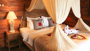 A bed with a canopy, pillows, a bedside table with a lamp, and a brick wall.