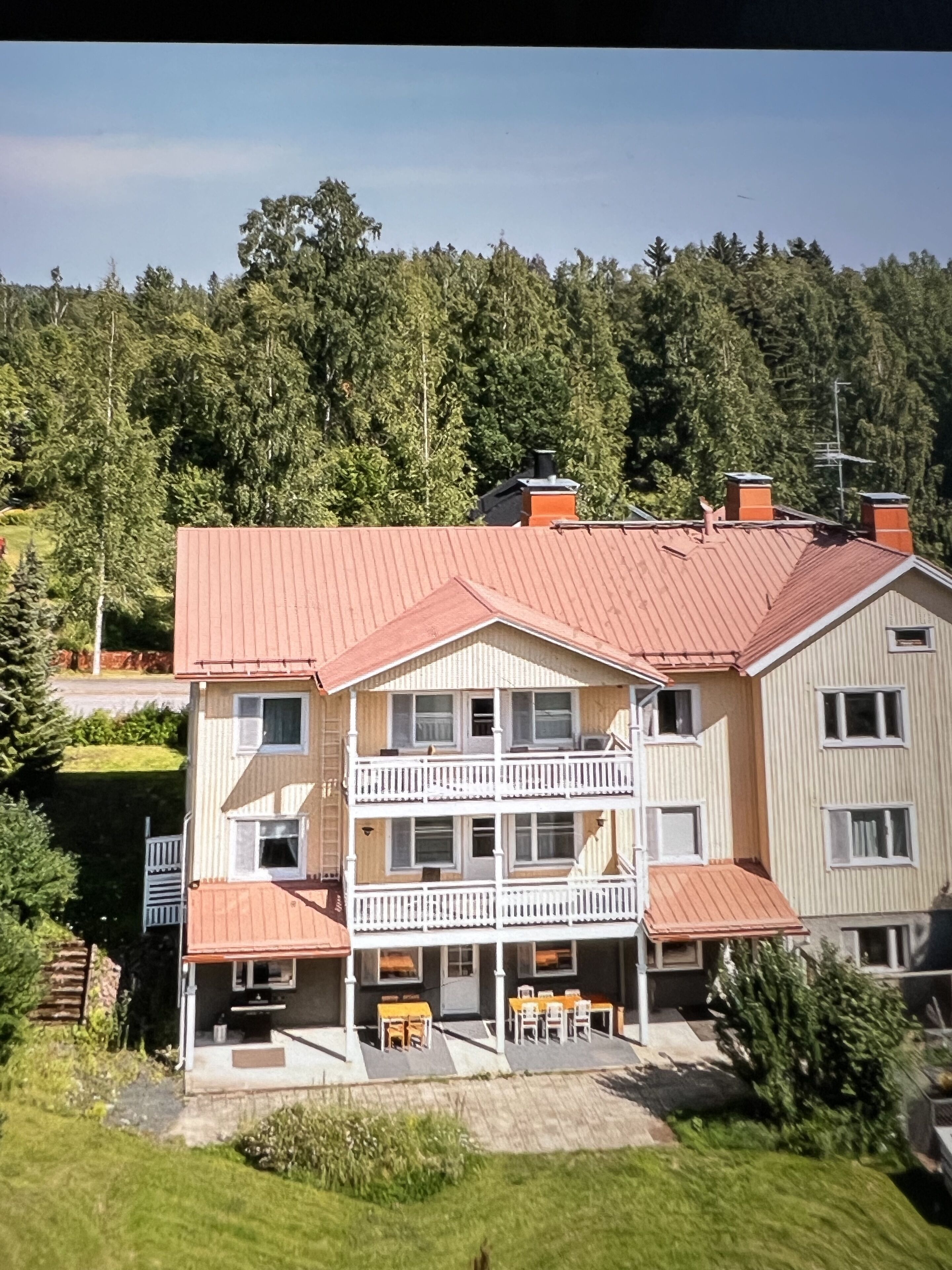 A two-story building with a red roof, multiple balconies, and a patio area with outdoor seating.