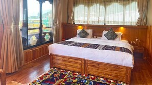 A bedroom with a wooden bed, a window with curtains, and a view of a building outside. - Pema Yangsel Hotel (Paro)