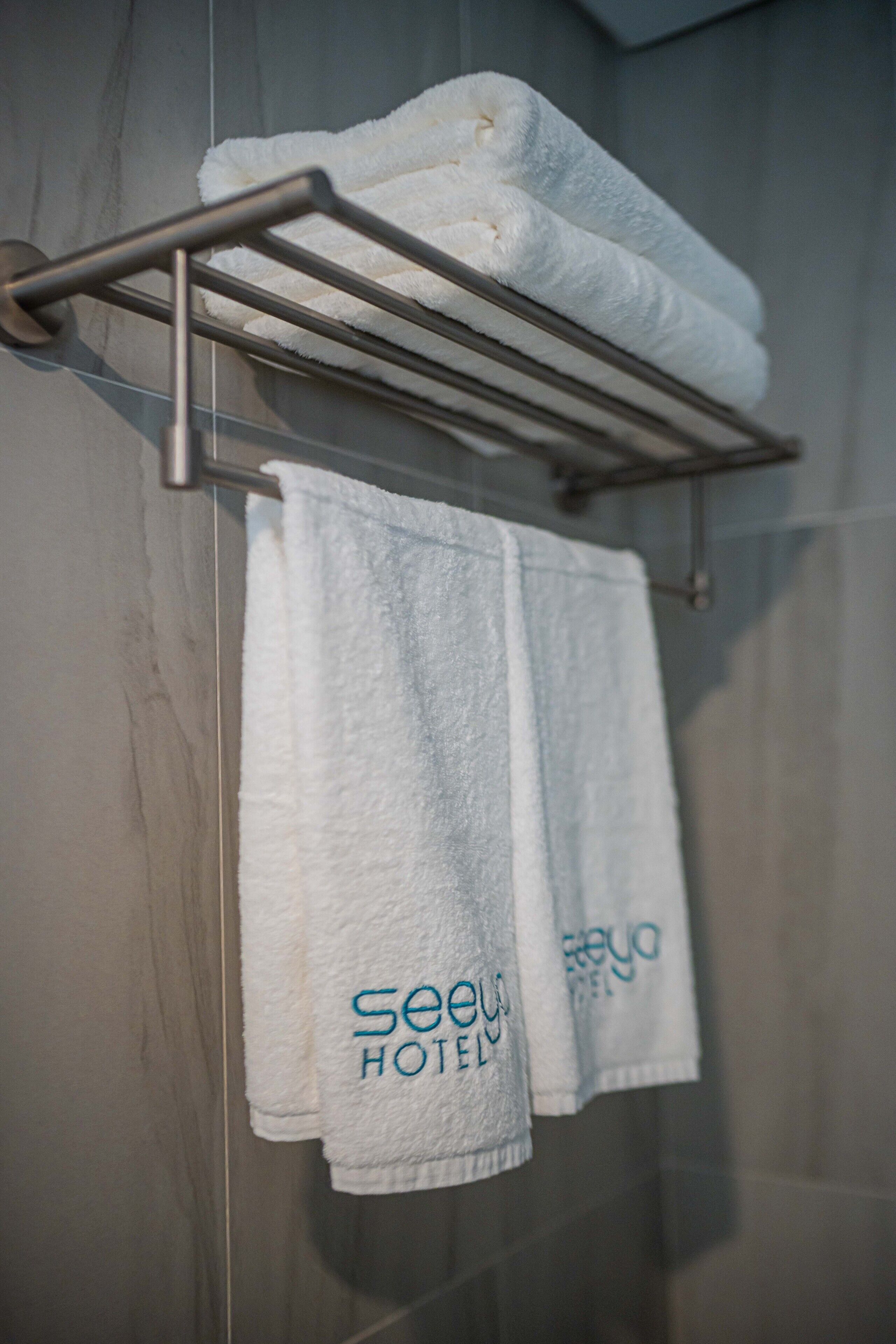 A bathroom with a towel rack holding two white towels and a metal towel holder with three folded towels.