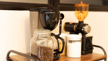 Eine Kaffeemaschine, eine Kaffeemühle und ein Glas mit Kaffeebohnen auf einem Holzboden.