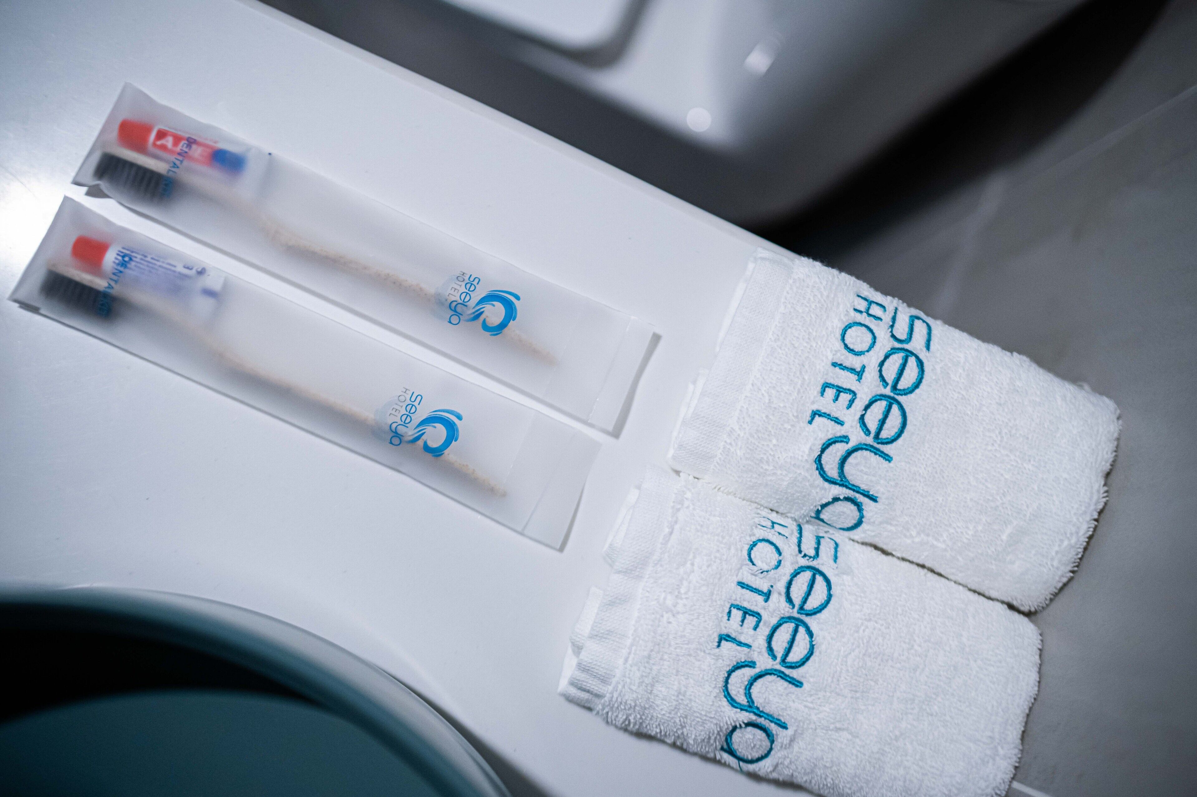 A white towel with "500 Hotel" embroidered in blue, a toothbrush, and a tube of toothpaste on a white surface.