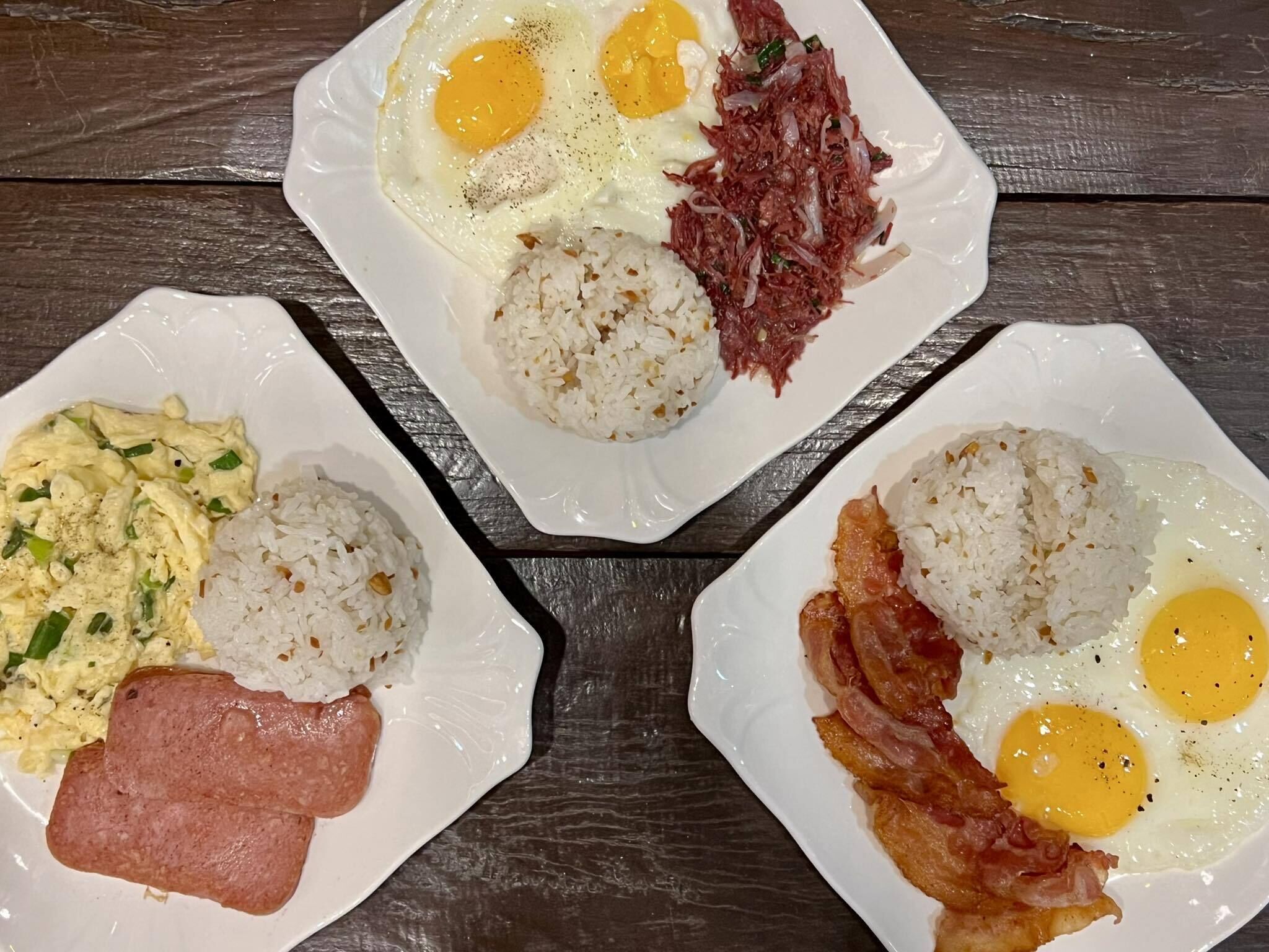 Three plates of breakfast food including eggs, rice, and meat.
