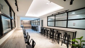 Een moderne congreszaal met een lange tafel, meerdere stoelen, grote ramen en een plafondlamp.