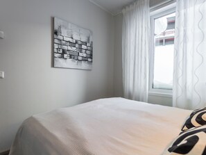 Een slaapkamer met een bed, een raam met gordijnen en een kunstwerk aan de muur.