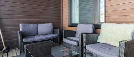 Un patio con mobiliario de mimbre, incluyendo un sofá y sillas, además de una mesa de centro de vidrio.