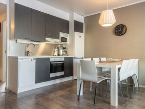 Une cuisine moderne avec un coin repas, comprenant une table blanche, des meubles gris et un luminaire suspendu.