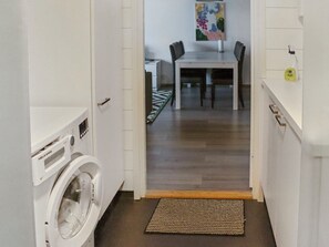 Ett tvättrum med tvättmaskin, en matplats med bord och stolar samt en mönstrad matta på golvet.