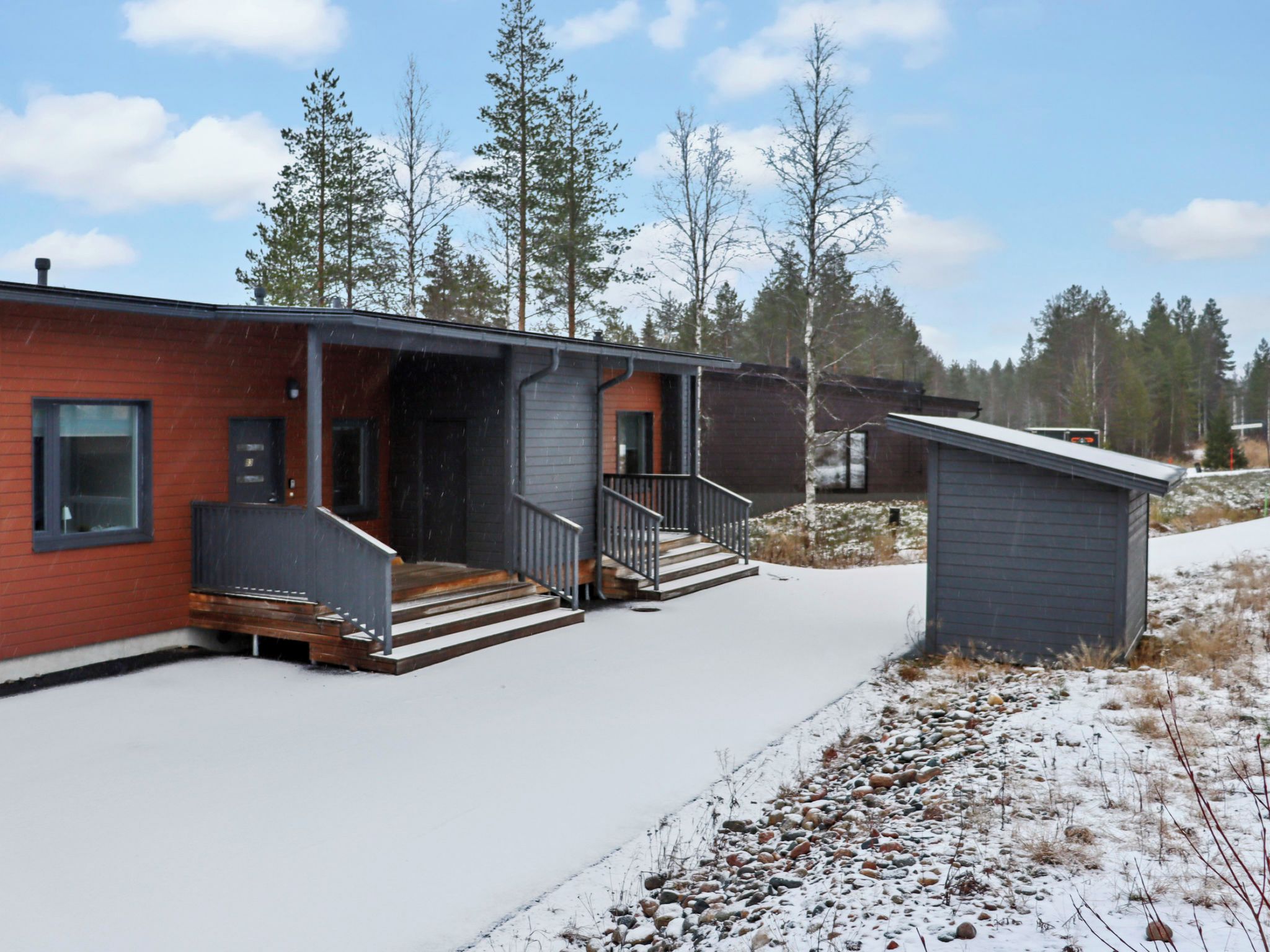 Un bâtiment moderne à deux étages, avec une façade en briques rouges, un porche couvert et un petit abri adjacent.