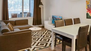 Una sala de estar moderna con sofá, mesa de comedor, sillas, televisor y vista a la montaña a través de la ventana.