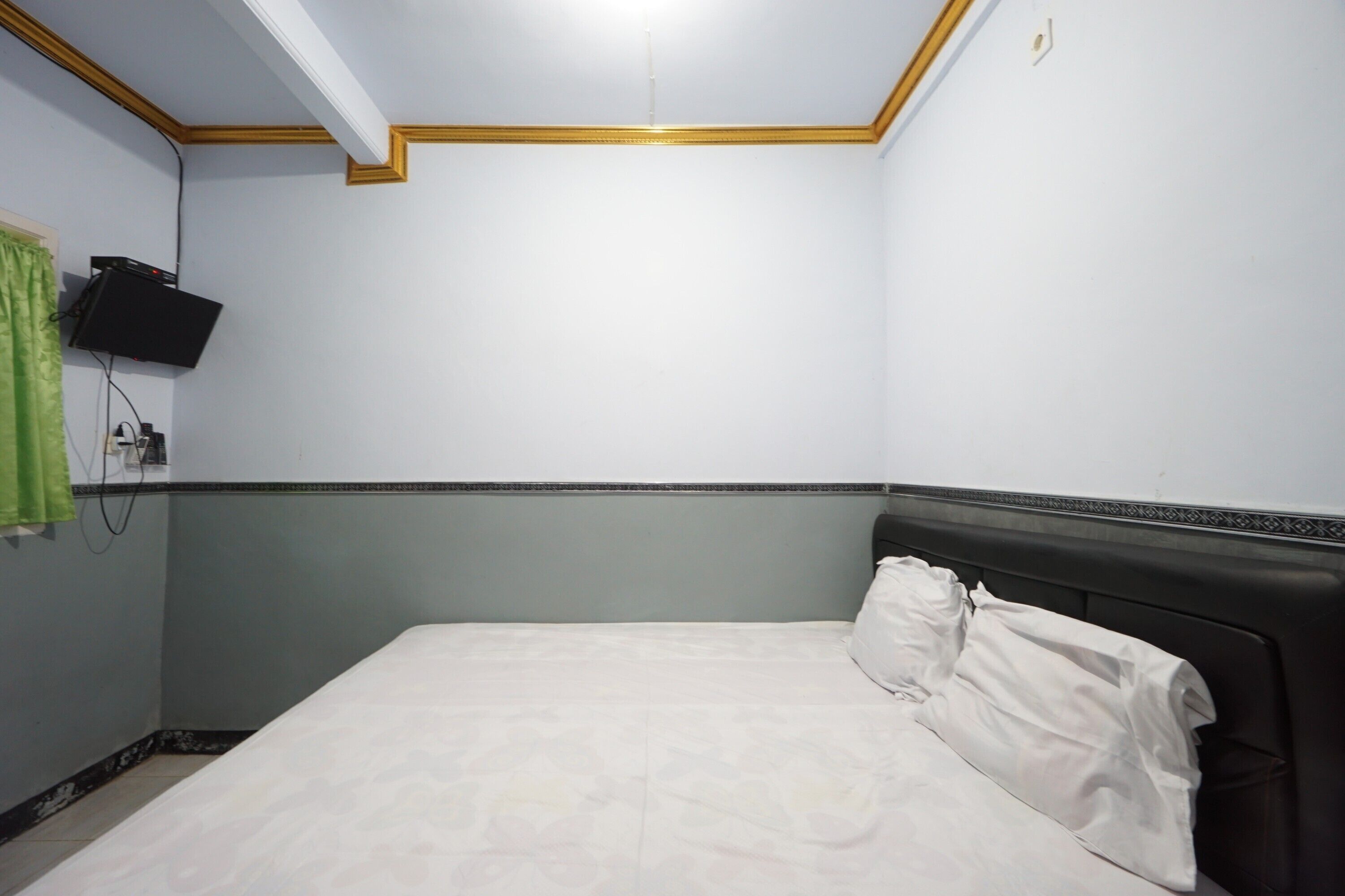 Una habitación con una cama, un televisor montado en la pared y una cortina verde.