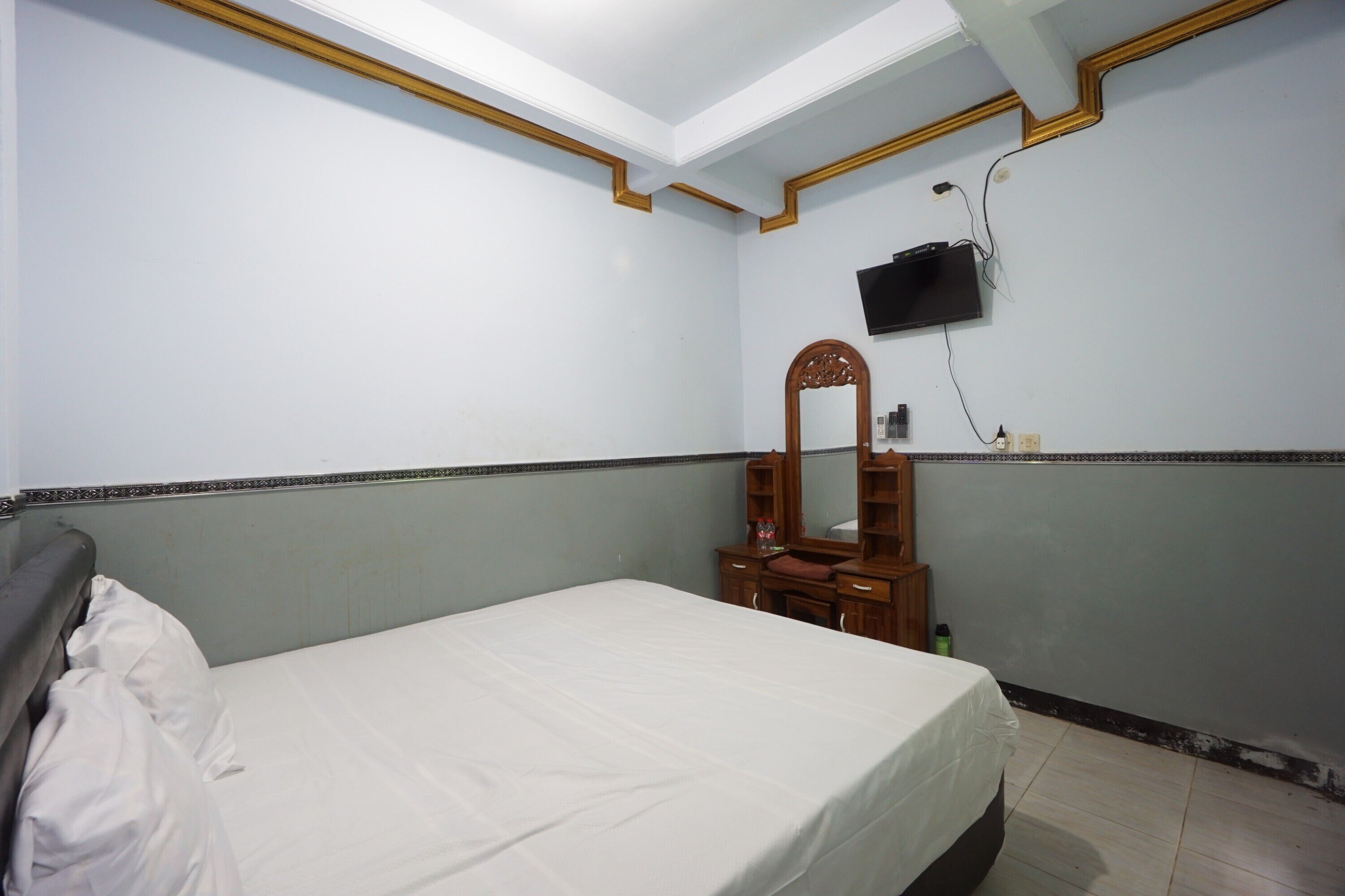A bedroom with a bed, a dresser, a mirror, and a television mounted on the wall.