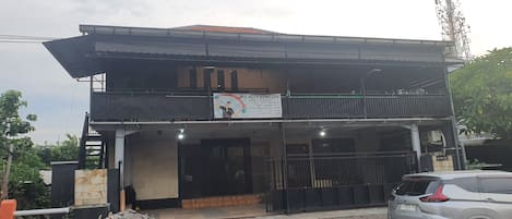 A two-story building with a signboard, a gated entrance, and a parked car.