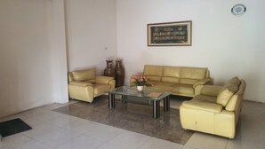 A living room with two beige sofas, a glass coffee table, and a framed calligraphy piece on the wall. - OYO 93623 Assalam Homestay Syariah (Surabaya)