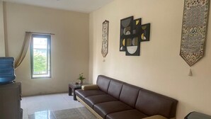 A living room with a brown sofa, a water dispenser, a small table with a plant, and decorative wall hangings. - OYO 93623 Assalam Homestay Syariah (Surabaya)