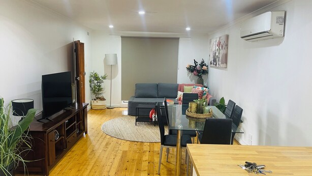 A modern living room with a TV, sofa, and dining area. - Home in Sunshine  (Sunshine)