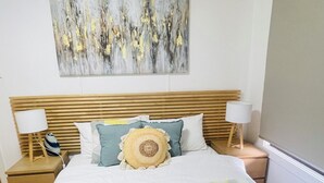 A neatly made bed with a green knitted blanket, a wooden headboard, and a gray abstract painting above it. - Home in Sunshine  (Sunshine)