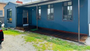 A small, single-story house with a dark blue exterior, a front porch, and a garage door. - Home in Sunshine  (Sunshine)