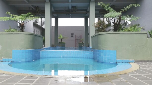 A swimming pool with a blue tiled edge, surrounded by a low wall and potted plants. - Hotel O Apartment Grand Asia Afrika By Prisma (Bandung)
