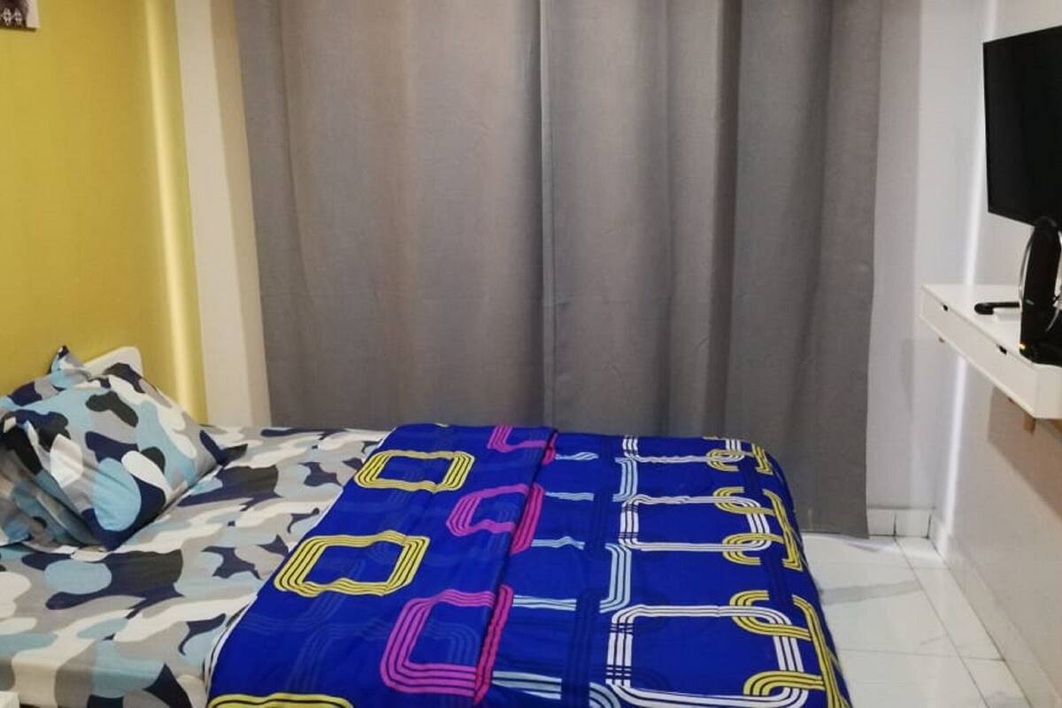 Ein Schlafzimmer mit einem Bett, einem Fernseher auf einem Schrank und einem Vorhang.