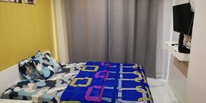 A bedroom with a bed, a television on a stand, and a curtain. - Hotel O Apartment Grand Asia Afrika By Prisma (Bandung)