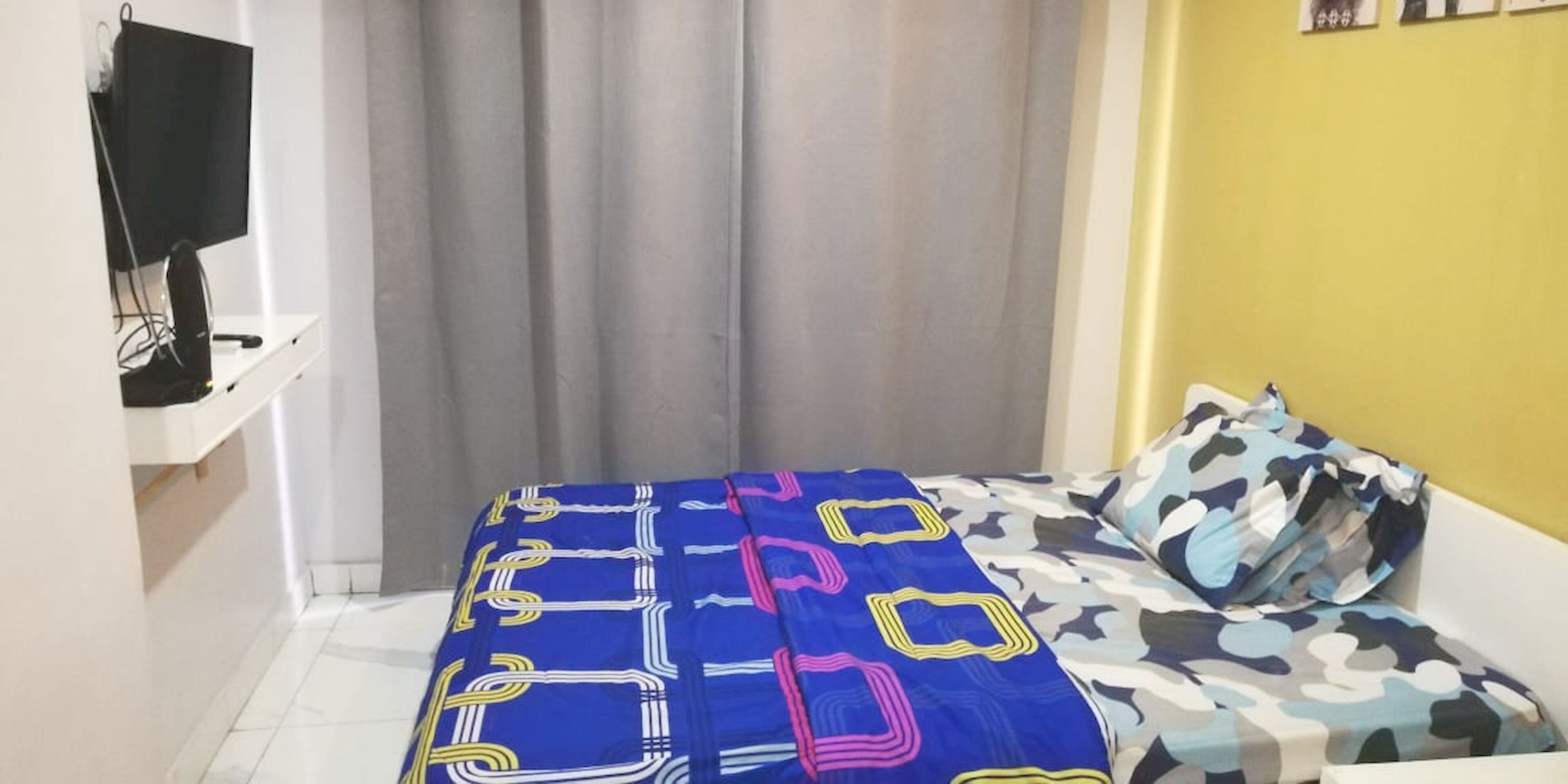 Une chambre à coucher avec un lit, un téléviseur posé sur un meuble et un rideau.