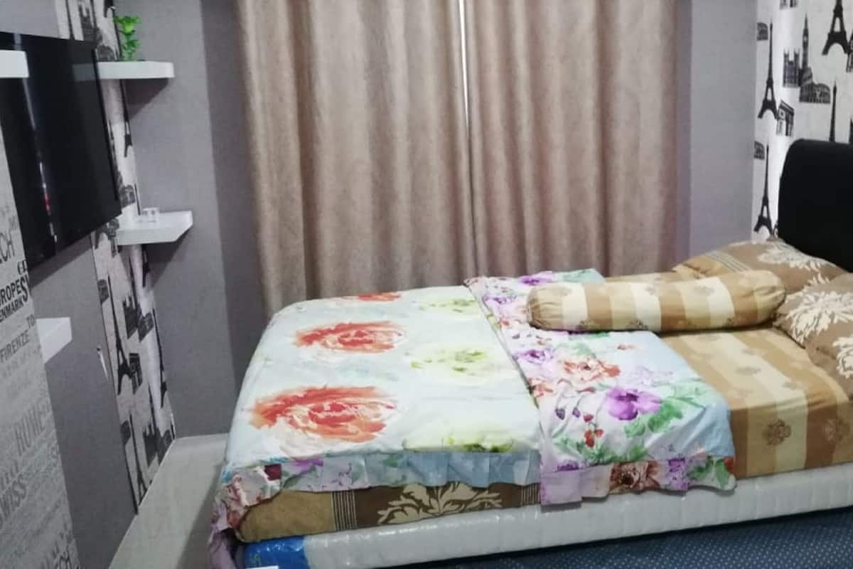 Ein Bett mit floraler Bettwäsche, einem schwarzen Kopfteil und einem Vorhang im Hintergrund.