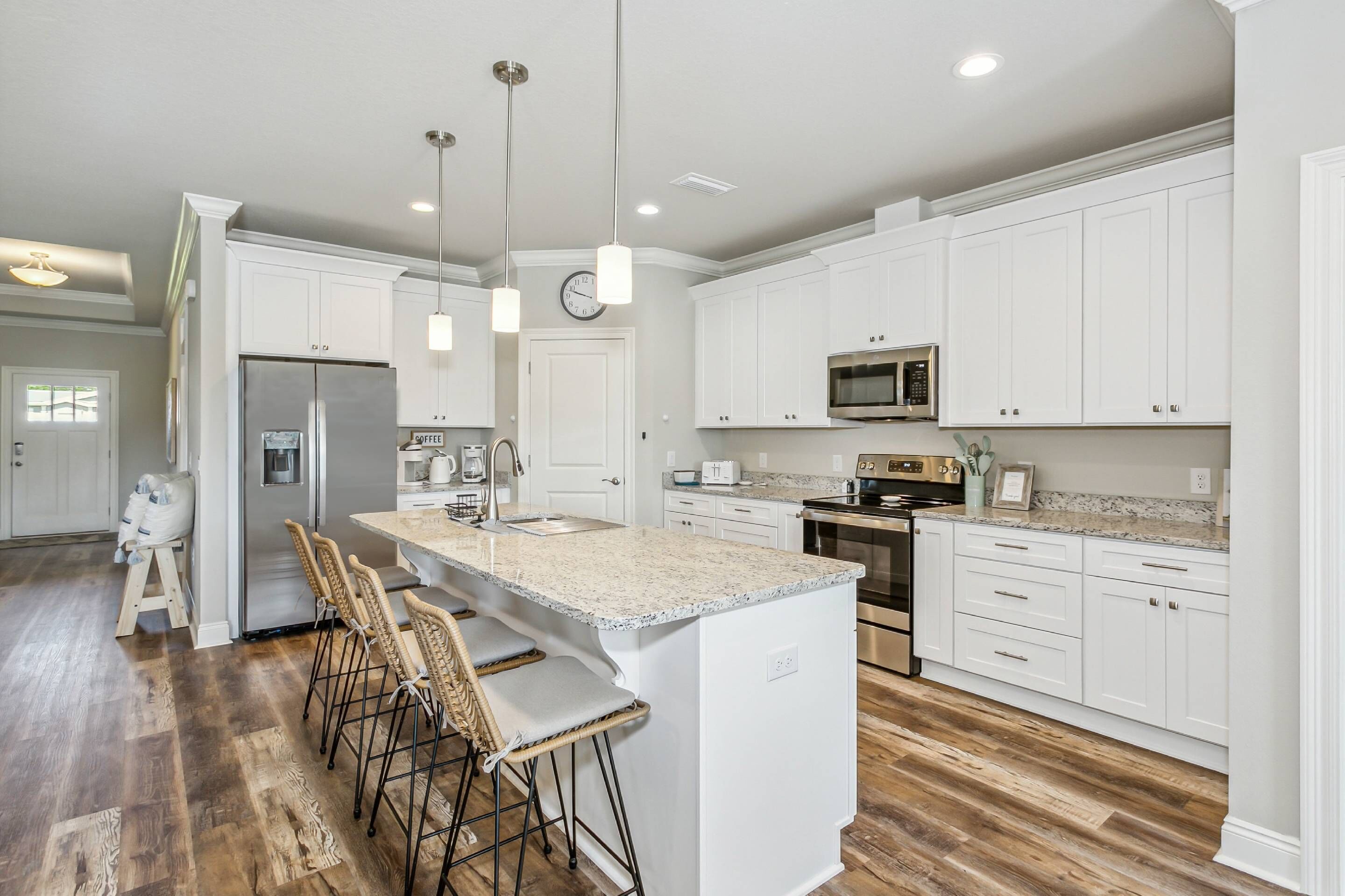 A modern kitchen with white cabinetry, a central island with bar stools, stainless steel appliances, and a clock on the wall.