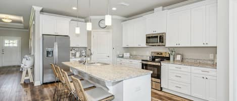 A modern kitchen with white cabinetry, a central island with bar stools, stainless steel appliances, and a clock on the wall.
