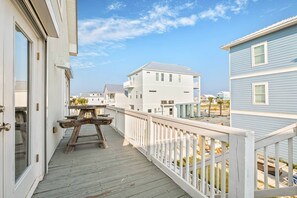 Eine Holzterrasse mit einer Holzbank, weißen Geländern und Blick auf Strandhäuser.