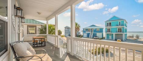 A covered porch with a view of a beach and two blue houses.