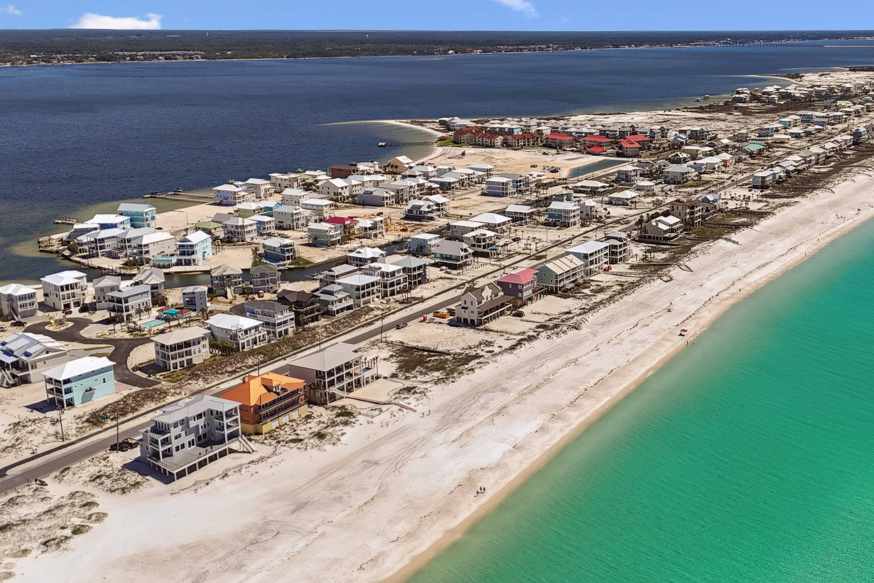 Una vista aerea di una zona residenziale costiera con case lungo la spiaggia, un molo che si protende nell'acqua e un cielo blu limpido.