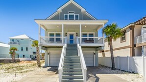 A two-story house with a front porch, a staircase leading to the entrance, and a white fence surrounding the property. - Gorgeous Sound-side Family Friendly Retreat l Golf Cart Included l Convenient to National Seashore (Navarre)