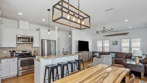 A modern kitchen with a central island, bar stools, stainless steel appliances, and a wooden dining table. - Gorgeous Sound-side Family Friendly Retreat l Golf Cart Included l Convenient to National Seashore (Navarre)