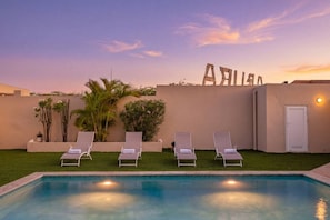 A swimming pool with lounge chairs and a wall with the word 'ARIES' in the background.