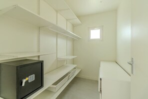 A small, white room with a metal safe, a window, and a white cabinet.